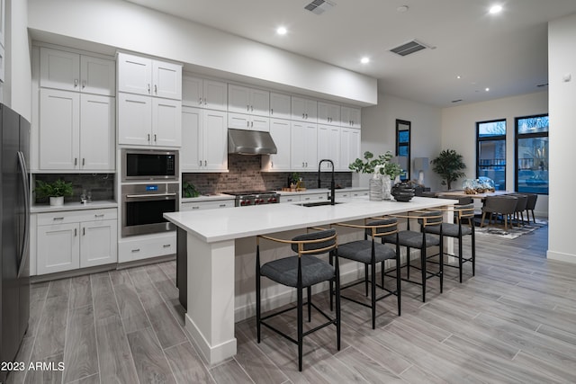 kitchen with a sink, oven, under cabinet range hood, built in microwave, and range