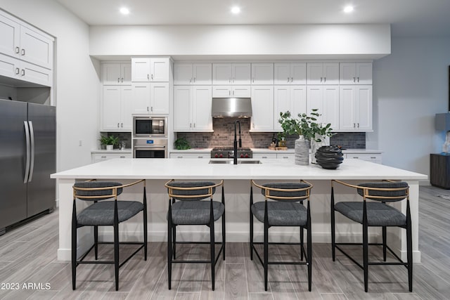 kitchen with a sink, light countertops, under cabinet range hood, appliances with stainless steel finishes, and tasteful backsplash