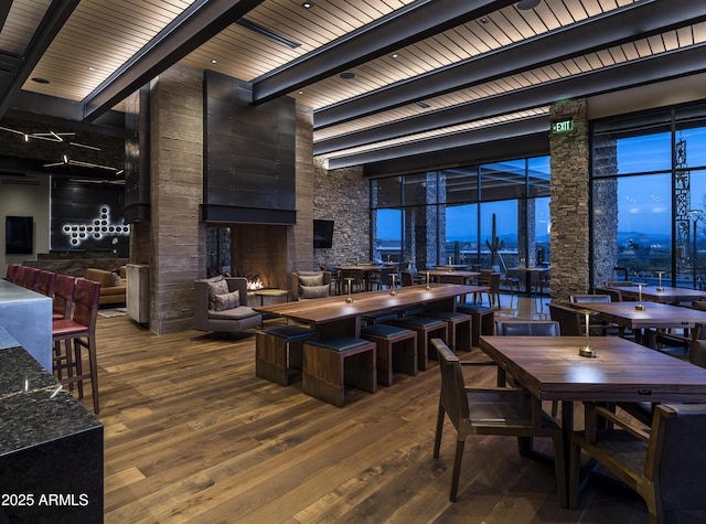 dining space with beamed ceiling, a high ceiling, and wood finished floors