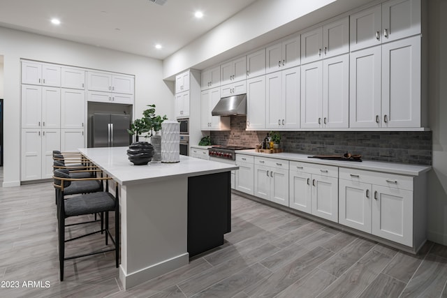 kitchen featuring a kitchen island, a breakfast bar, stainless steel appliances, under cabinet range hood, and backsplash