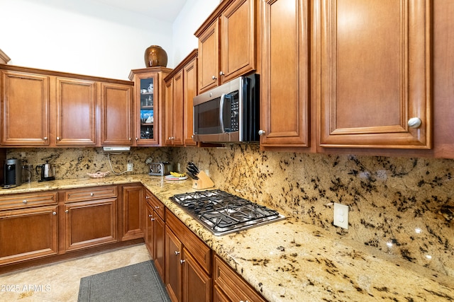 4229 E Nightingale Ln, Gilbert, AZ 85298 - kitchen with appliances with stainless steel finishes, tasteful backsplash, brown cabinetry, light stone counters, and glass insert cabinets