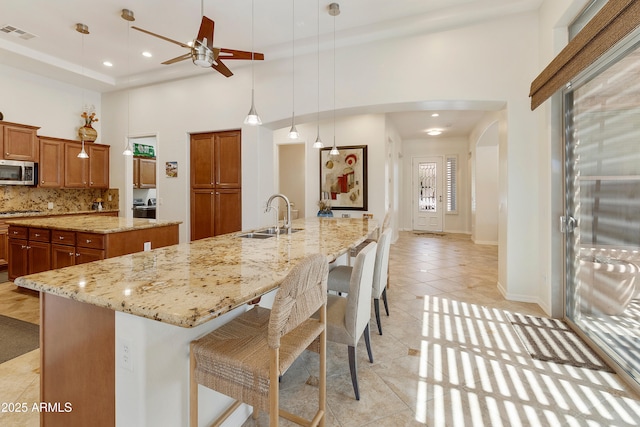 4229 E Nightingale Ln, Gilbert, AZ 85298 - kitchen with stainless steel microwave, a large island with sink, a high ceiling, brown cabinetry, and arched walkways