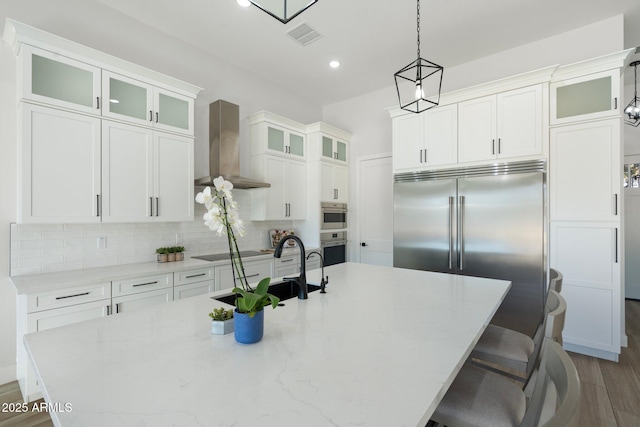 kitchen with a center island with sink, wall chimney range hood, and appliances with stainless steel finishes