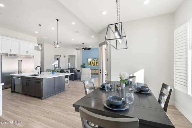 dining room with ceiling fan, sink, light hardwood / wood-style flooring, and vaulted ceiling