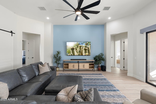 living room featuring ceiling fan, a barn door, and light wood-type flooring