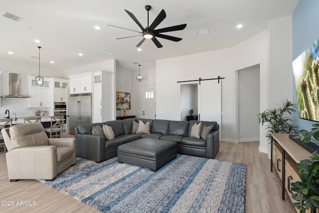 living room featuring ceiling fan, sink, a barn door, and light wood-type flooring