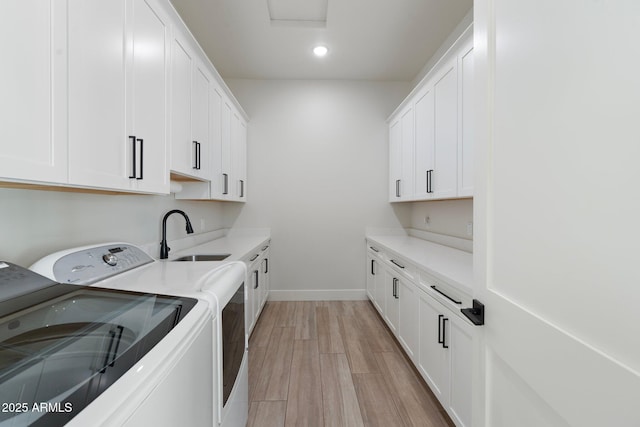 clothes washing area featuring cabinets, sink, washing machine and clothes dryer, and light hardwood / wood-style floors