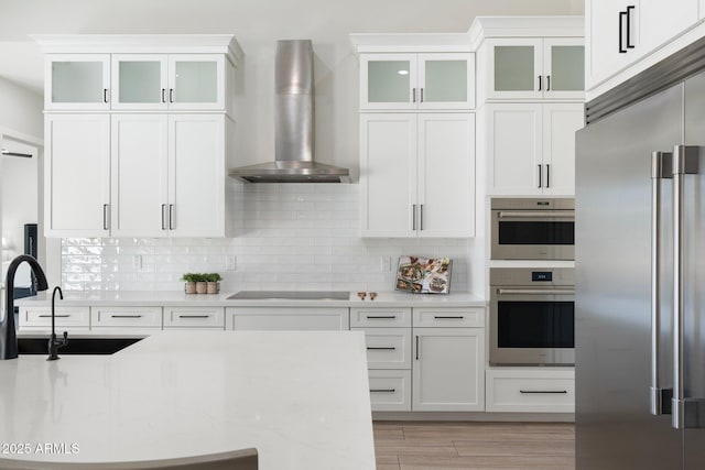 kitchen with white cabinetry, wall chimney range hood, stainless steel appliances, and tasteful backsplash