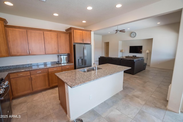 kitchen with stainless steel fridge, brown cabinets, a sink, stove, and light stone countertops