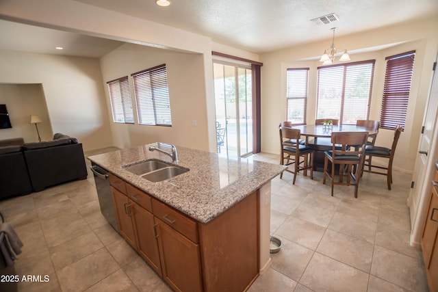 kitchen with brown cabinetry, hanging light fixtures, visible vents, a sink, and a center island with sink