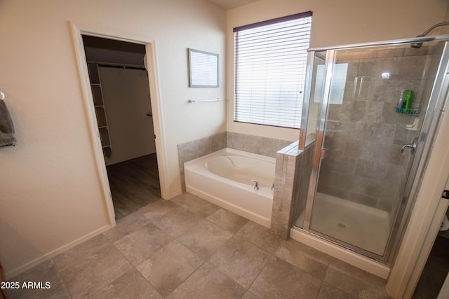 bathroom with a walk in closet, a garden tub, baseboards, and a stall shower