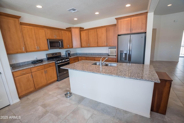 kitchen featuring a sink, stainless steel appliances, a center island with sink, and brown cabinets