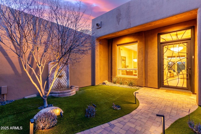 view of exterior entry with a lawn and stucco siding