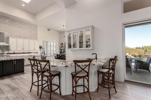 30600 N Pima Rd Unit 49, Scottsdale, AZ 85266 - kitchen featuring light stone countertops, a breakfast bar area, a peninsula, white cabinets, and wall chimney exhaust hood