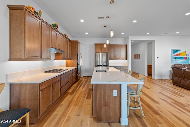 kitchen with appliances with stainless steel finishes, light wood-type flooring, a spacious island, sink, and hanging light fixtures