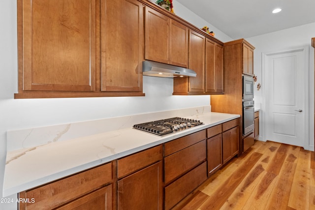 kitchen with light stone countertops, stainless steel appliances, and light hardwood / wood-style flooring