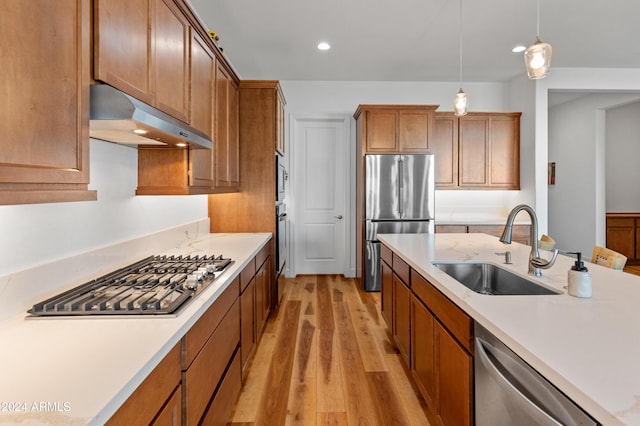 kitchen with stainless steel appliances, sink, pendant lighting, and light wood-type flooring