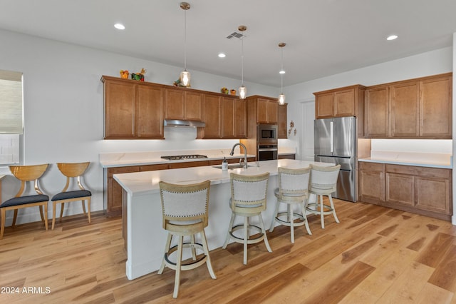 kitchen with sink, hanging light fixtures, light hardwood / wood-style flooring, a center island with sink, and appliances with stainless steel finishes