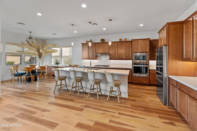 kitchen featuring pendant lighting, a breakfast bar, an island with sink, light hardwood / wood-style floors, and stainless steel appliances