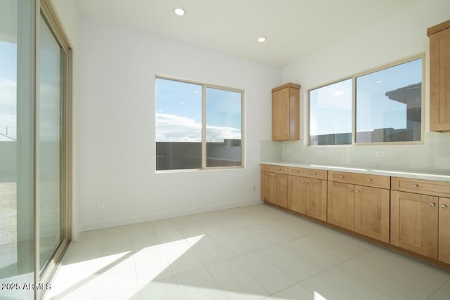 kitchen featuring baseboards, recessed lighting, light countertops, brown cabinets, and backsplash