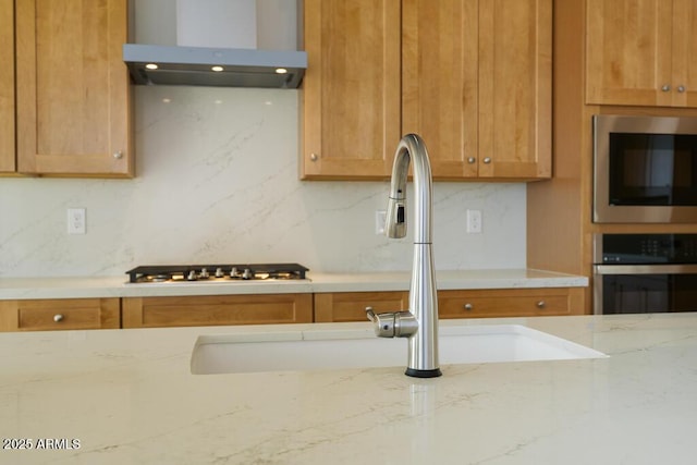 kitchen with backsplash, light stone countertops, appliances with stainless steel finishes, island exhaust hood, and a sink