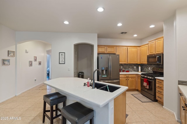 kitchen with an island with sink, decorative backsplash, sink, stainless steel fridge, and gas range