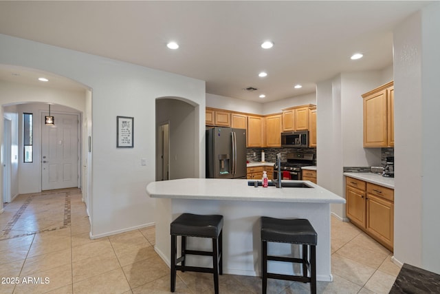 kitchen featuring light tile patterned floors, a center island with sink, stainless steel appliances, and tasteful backsplash