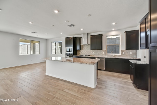 kitchen with stainless steel appliances, a center island, light stone countertops, and wall chimney exhaust hood