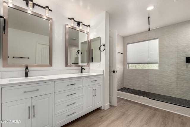 full bath with double vanity, a walk in shower, a sink, and wood finished floors