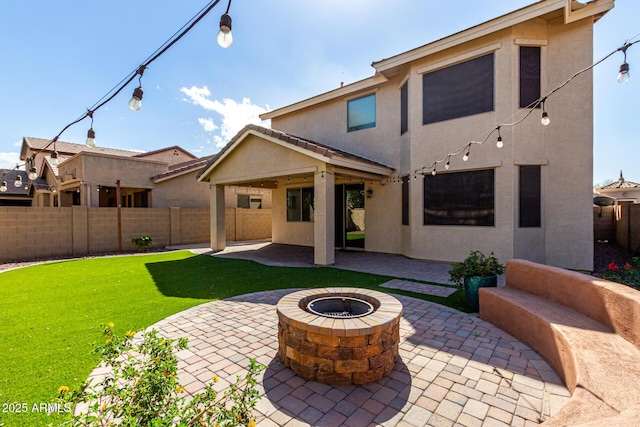 rear view of property with stucco siding, a lawn, a patio area, a fenced backyard, and a fire pit