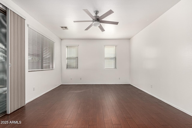 empty room with dark wood-style floors, ceiling fan, visible vents, and baseboards