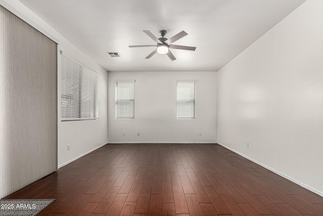 empty room with ceiling fan, dark wood finished floors, visible vents, and baseboards