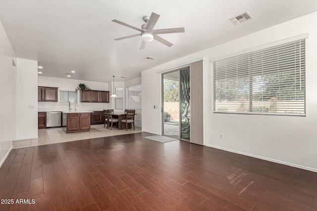 unfurnished living room with visible vents, ceiling fan, a sink, wood finished floors, and baseboards