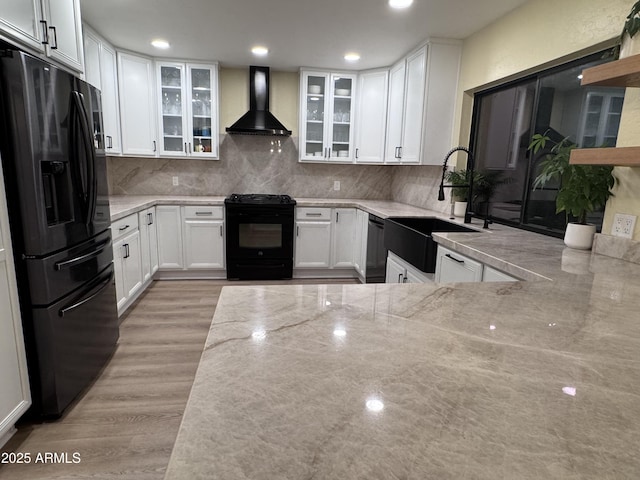 kitchen featuring white cabinetry, sink, light stone counters, black appliances, and wall chimney exhaust hood