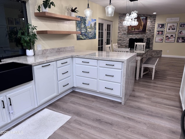 kitchen with white cabinetry, sink, hanging light fixtures, kitchen peninsula, and light hardwood / wood-style flooring