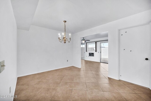 tiled spare room featuring ceiling fan with notable chandelier