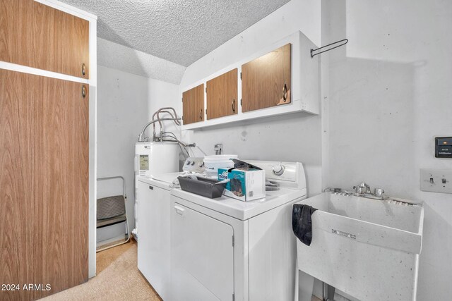 washroom with cabinets, light carpet, a textured ceiling, washer and dryer, and sink