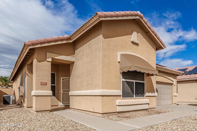 view of front of property with a tile roof, a garage, central AC, and stucco siding