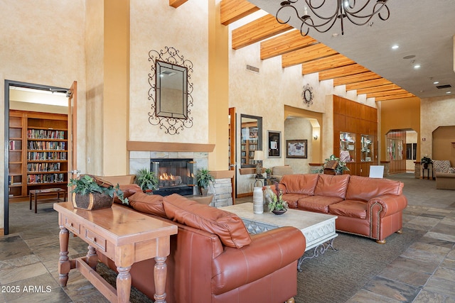 living room featuring built in shelves, an inviting chandelier, a tile fireplace, beamed ceiling, and a towering ceiling