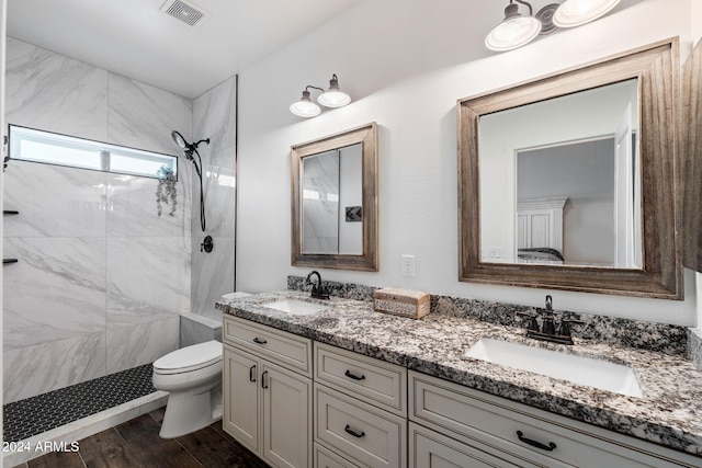 bathroom featuring a tile shower, vanity, wood-type flooring, and toilet