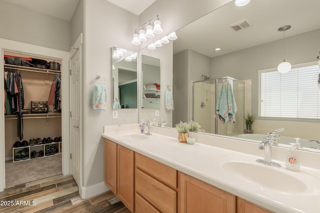 full bathroom featuring wood finished floors, a shower stall, double vanity, and a walk in closet