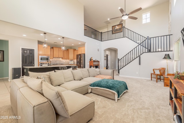 living room with arched walkways, ceiling fan, a high ceiling, stairway, and baseboards