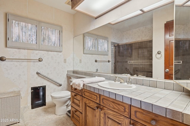 bathroom with toilet, a tile shower, and vanity