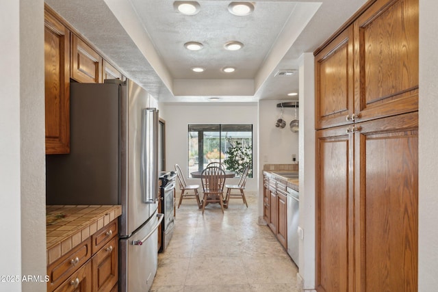 kitchen featuring appliances with stainless steel finishes, tile counters, brown cabinets, and a textured ceiling