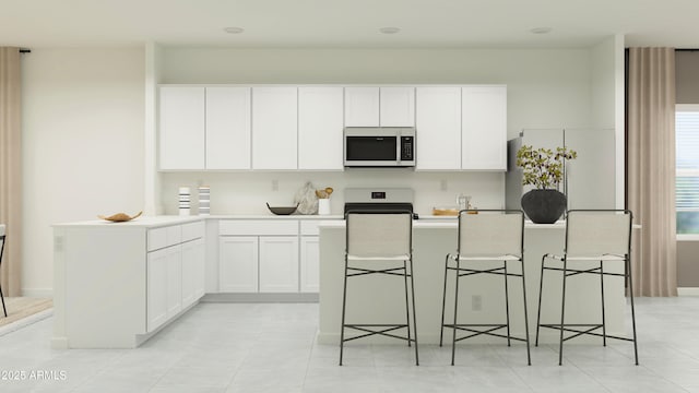 kitchen featuring light countertops, white cabinets, a kitchen breakfast bar, stainless steel microwave, and stove