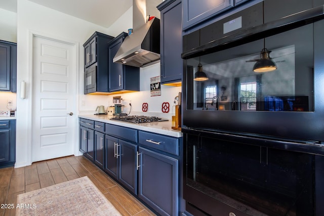 kitchen with stainless steel gas stovetop, wall chimney range hood, hanging light fixtures, blue cabinets, and double oven