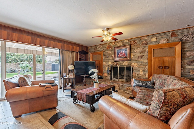 tiled living room with a fireplace, wood walls, and ceiling fan