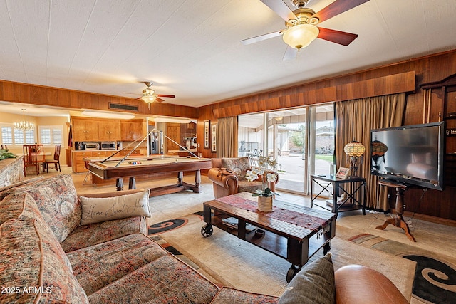 living room with ceiling fan with notable chandelier, light tile patterned flooring, and wood walls