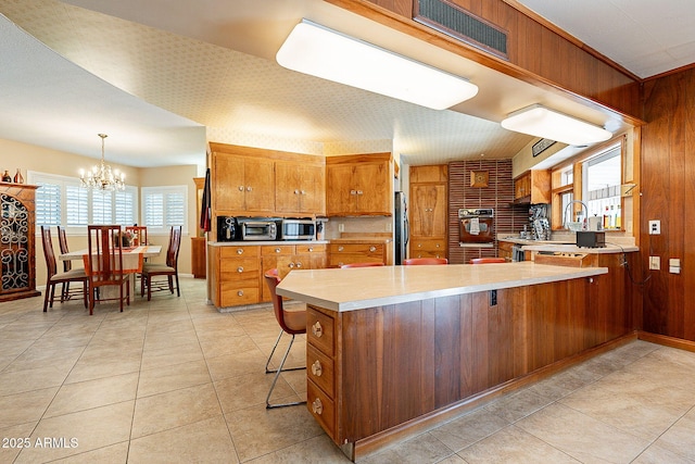 kitchen with wall oven, refrigerator, pendant lighting, a kitchen bar, and kitchen peninsula