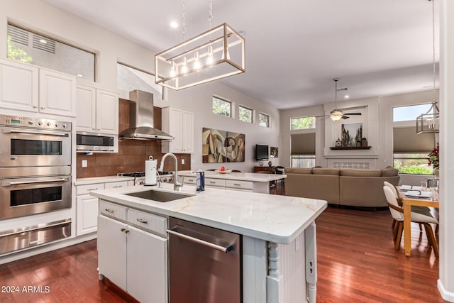 kitchen with wall chimney range hood, sink, an island with sink, white cabinetry, and stainless steel appliances